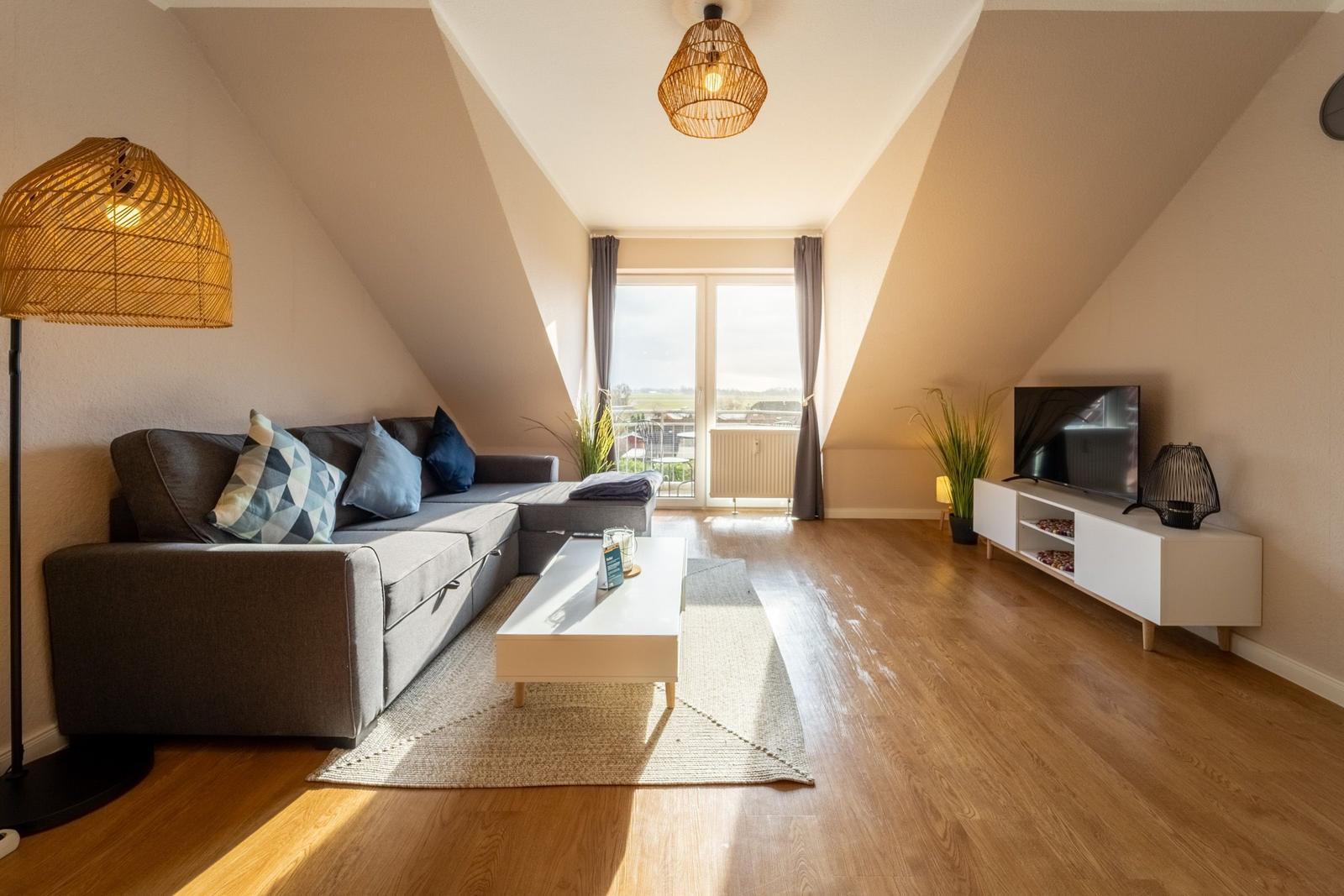 Wohnzimmer mit Sofa, Couchtisch und Fernseher. Holzboden und Dachschräge.