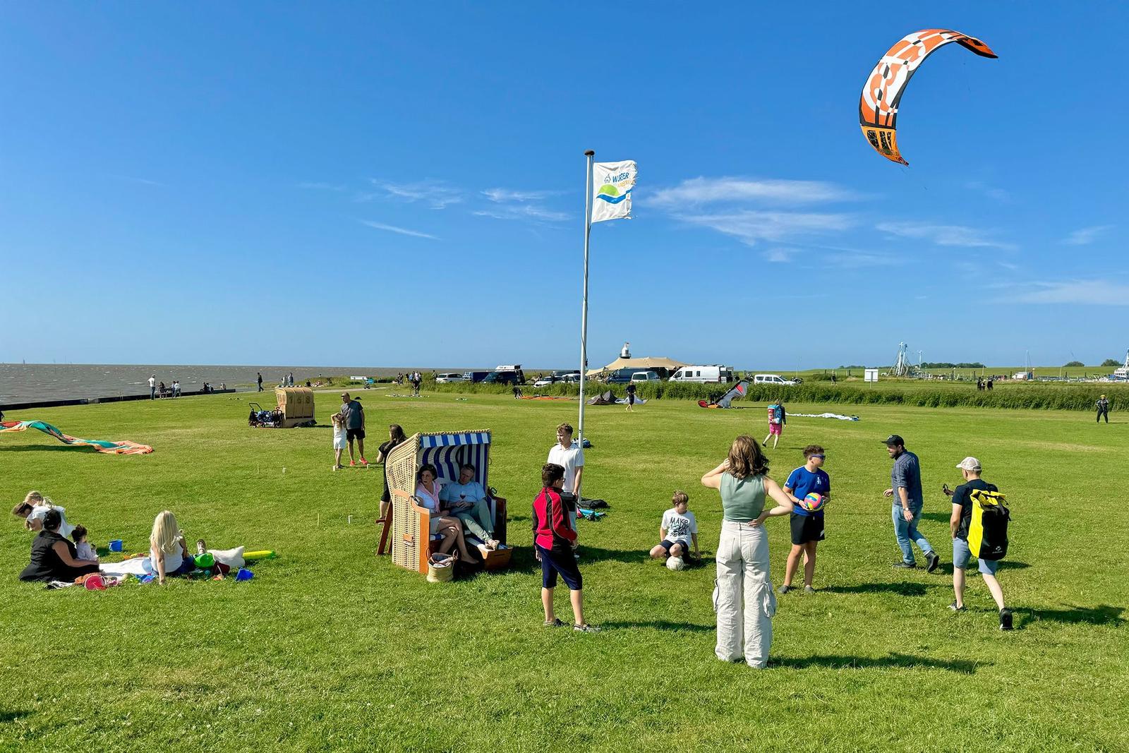 Grünes Feld am Strand mit Menschen, Strandkörben und einem Kitesurfer.
