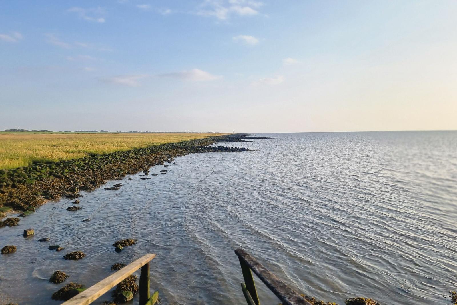 Meer und Wattlandschaft mit Steinschutz und Holzgeländer im Vordergrund.