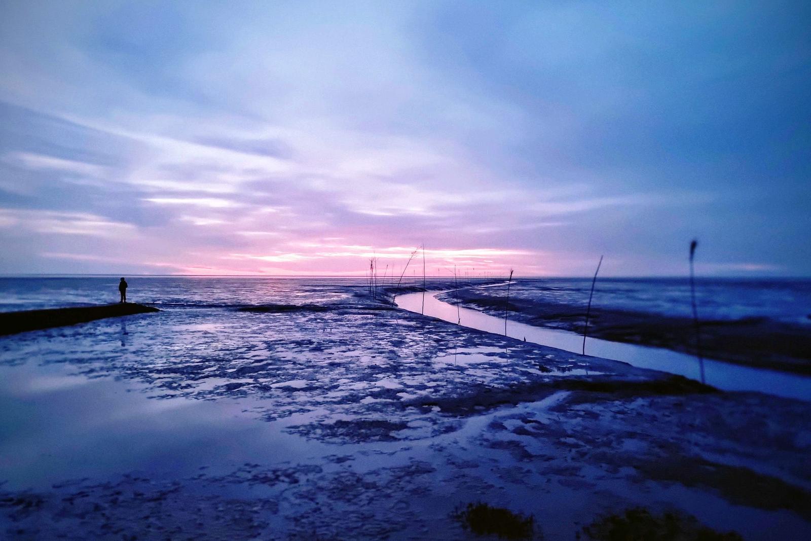 Ein Mensch steht am Ufer eines Flusses bei Sonnenuntergang mit farbigen Wolken.