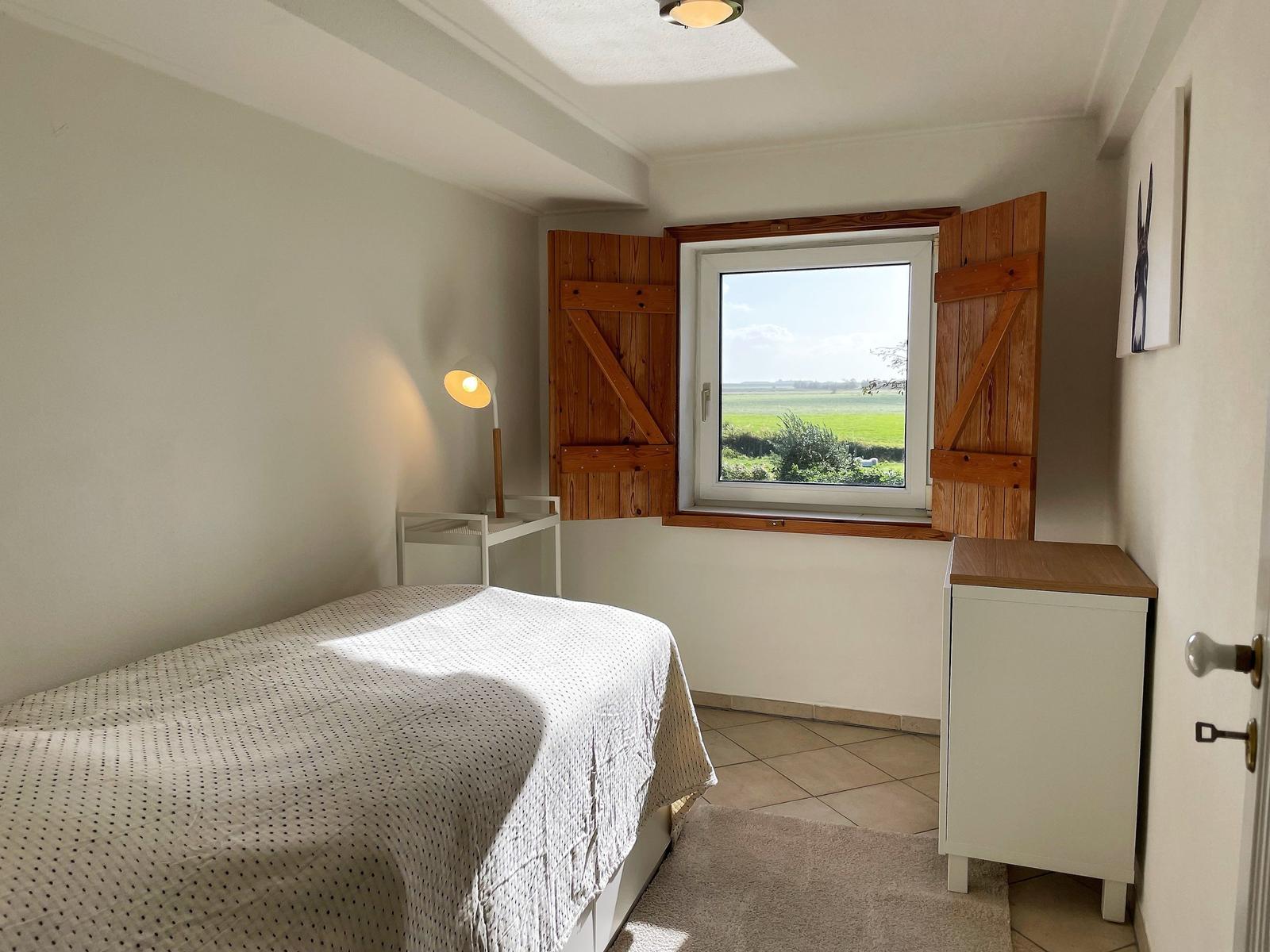 Bedroom with bed, window, and cabinet. Outside is a green landscape visible.