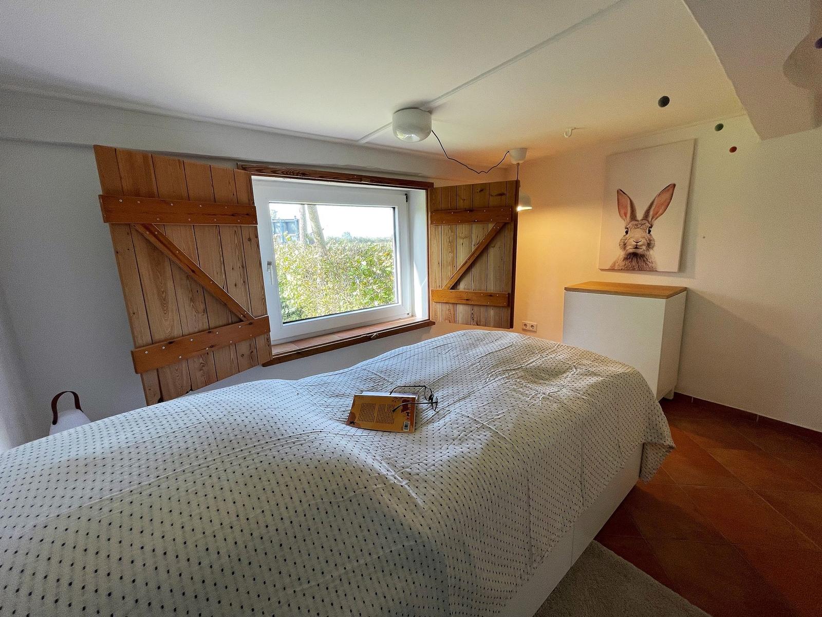 Bedroom with bed, window, and wall picture of a hare.