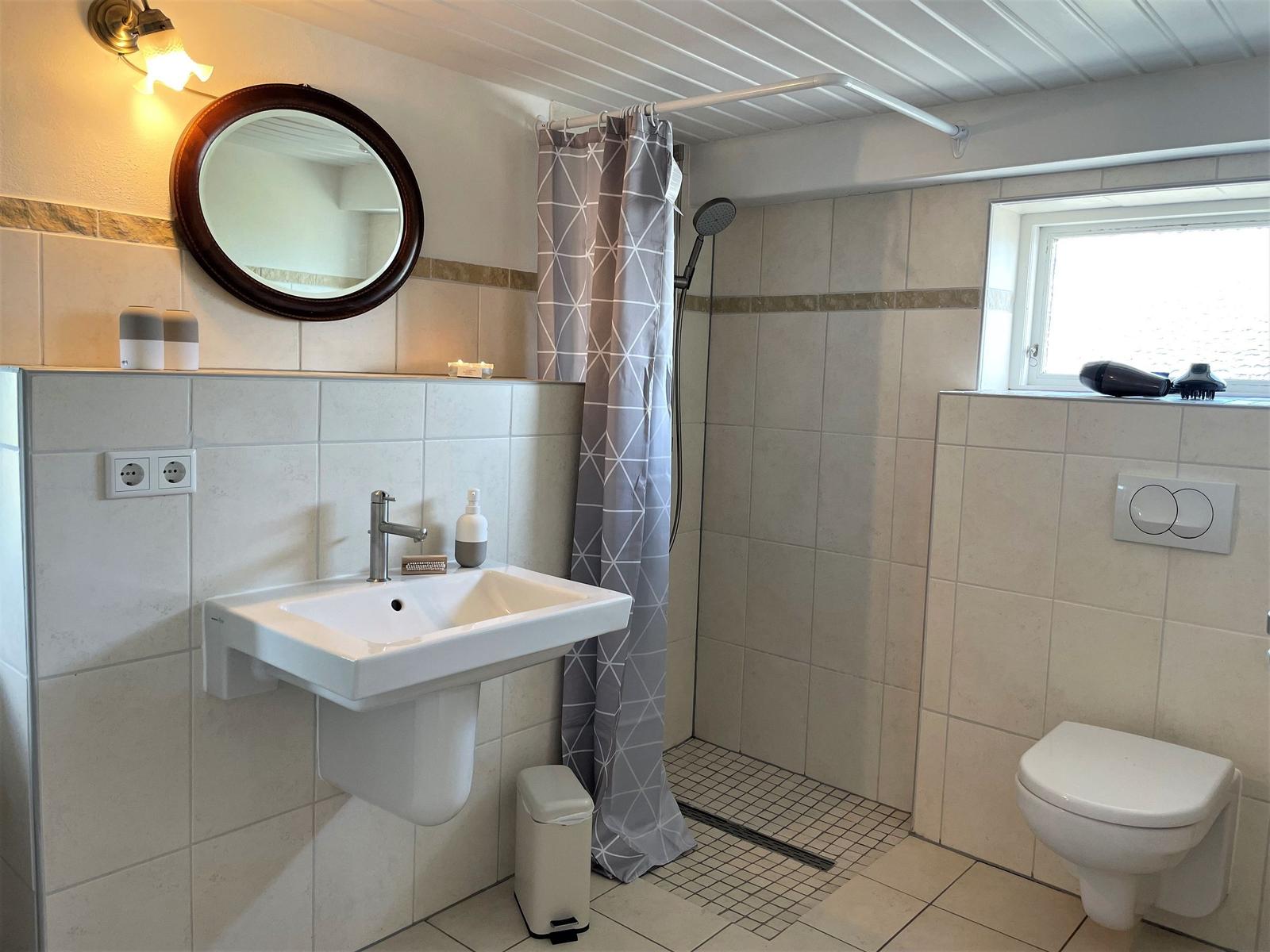 Bathroom with shower, sink, and toilet. Window, mirror, and shower curtain visible.