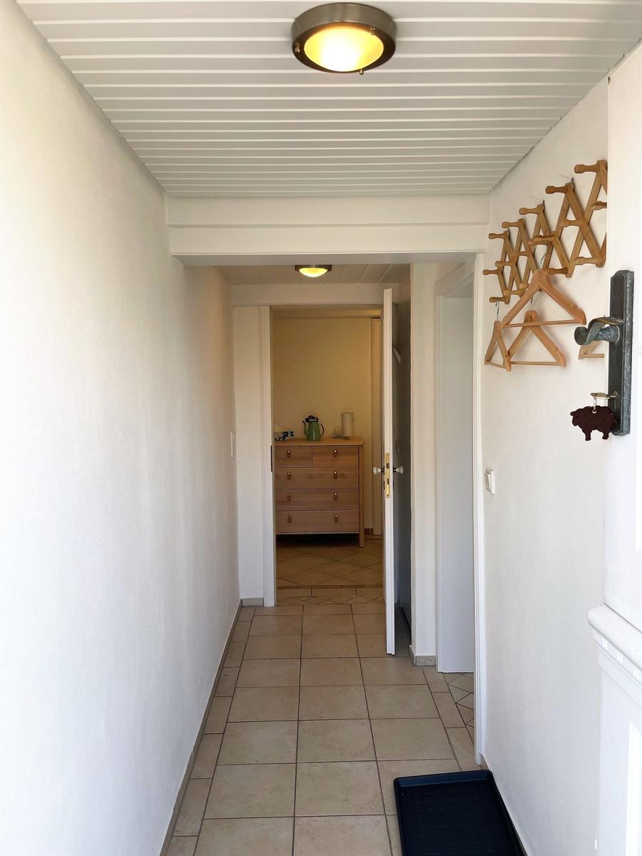 Hallway with wooden coat rack, door to bedroom, and tile floor