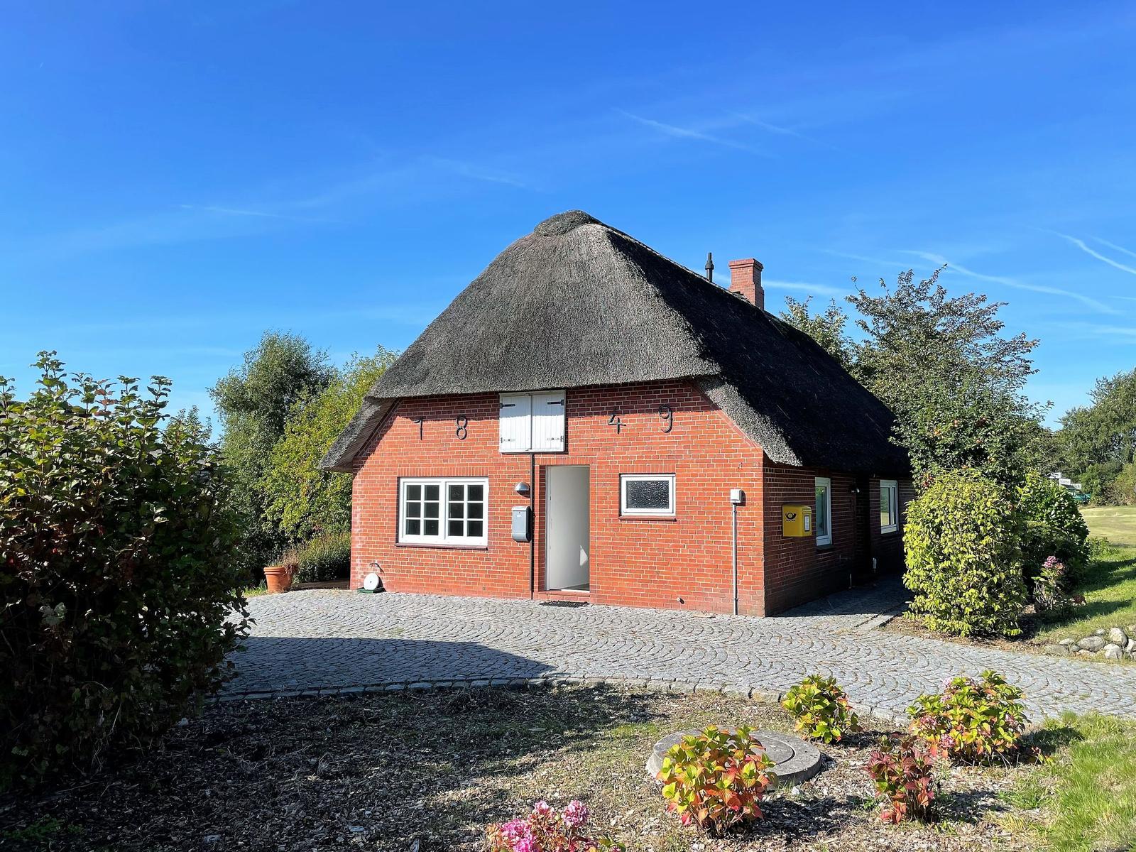 Red brick house with thatched roof and paved forecourt.