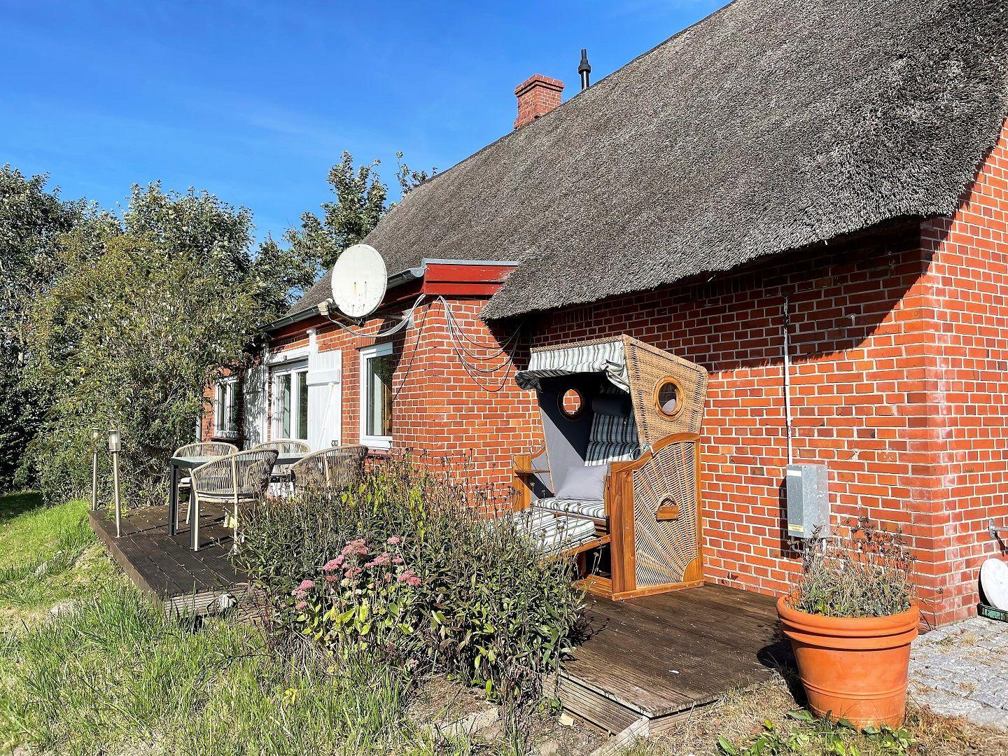 Red brick house with thatched roof, garden area with sun lounger and table