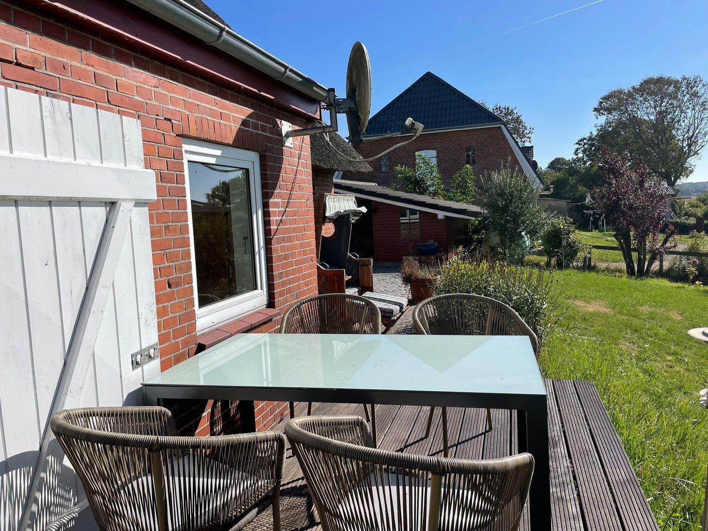 Terrace with table and chairs next to red brick house with garden.