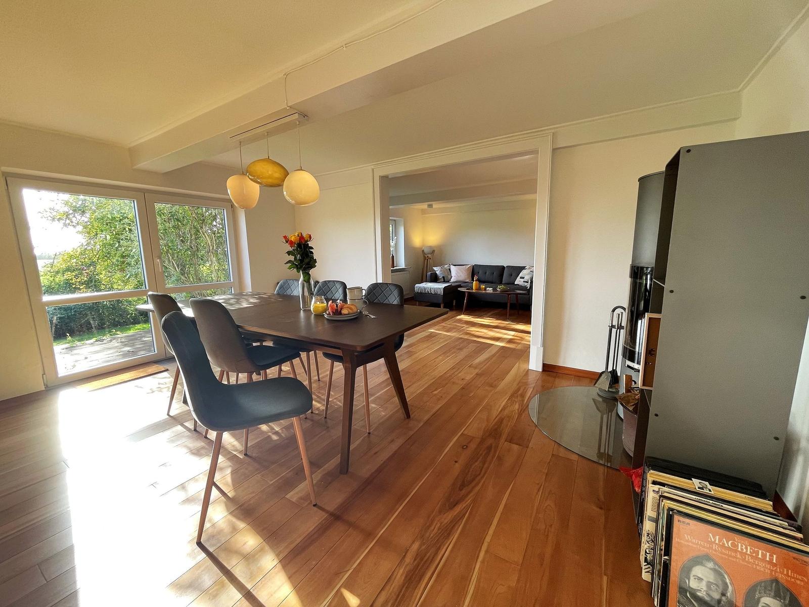 Dining area with table, chairs, and garden view. Living room in the background.