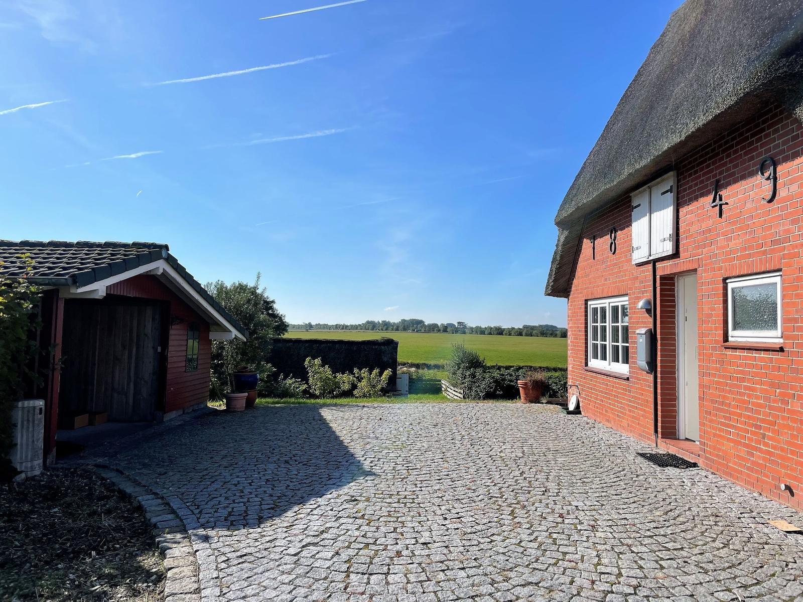 Red brick building with thatched roof and cobblestone path. Green fields in the background.