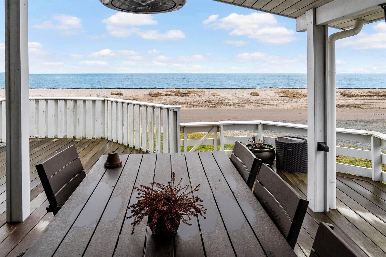 Terrasse mit Tisch und Stühlen, Blick auf Strand und Meer.