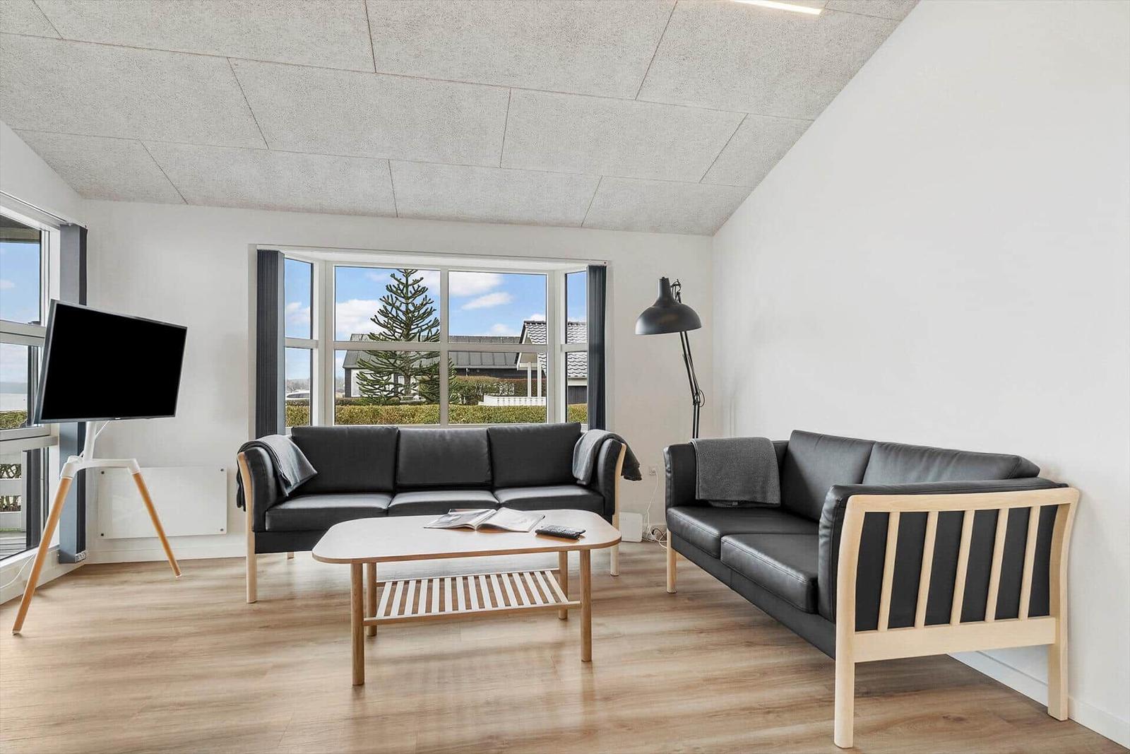 Wohnzimmer mit zwei Sofas, Couchtisch und TV. Große Fenster mit Blick auf Außenbereich.