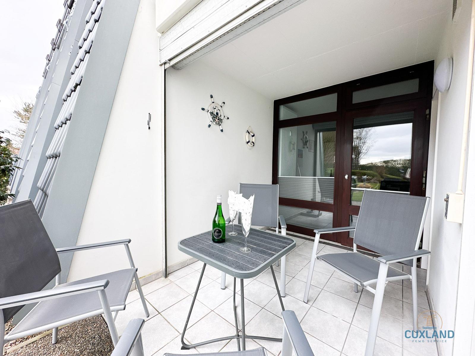 Terrasse mit Tisch, Stühlen und Flasche. Glasfront zur Wohnung.