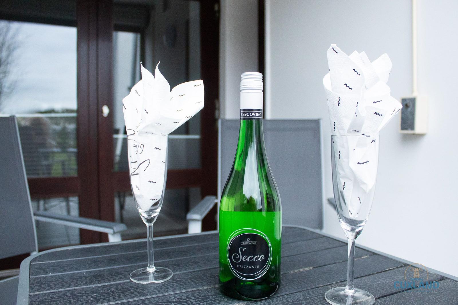 Auf der Terrasse stehen ein grünes Secco-Flasche und zwei Gläser mit Servietten.