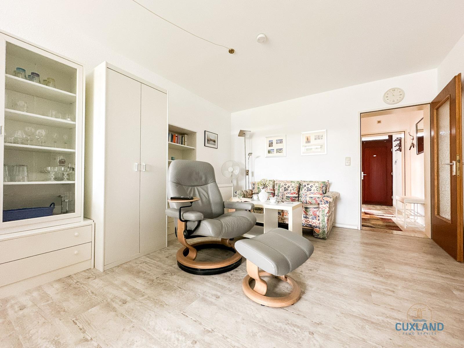 Wohnraum mit Sessel, Sofa und Glasvitrine. Holzfußboden und weiße Wände.