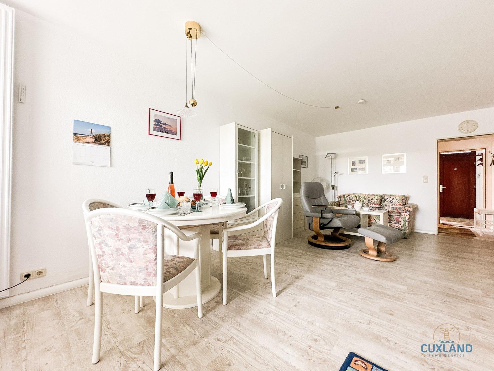 Essbereich mit Tisch und Stühlen, Wohnbereich mit Sofa und Sessel, helle Wände und Holzboden.