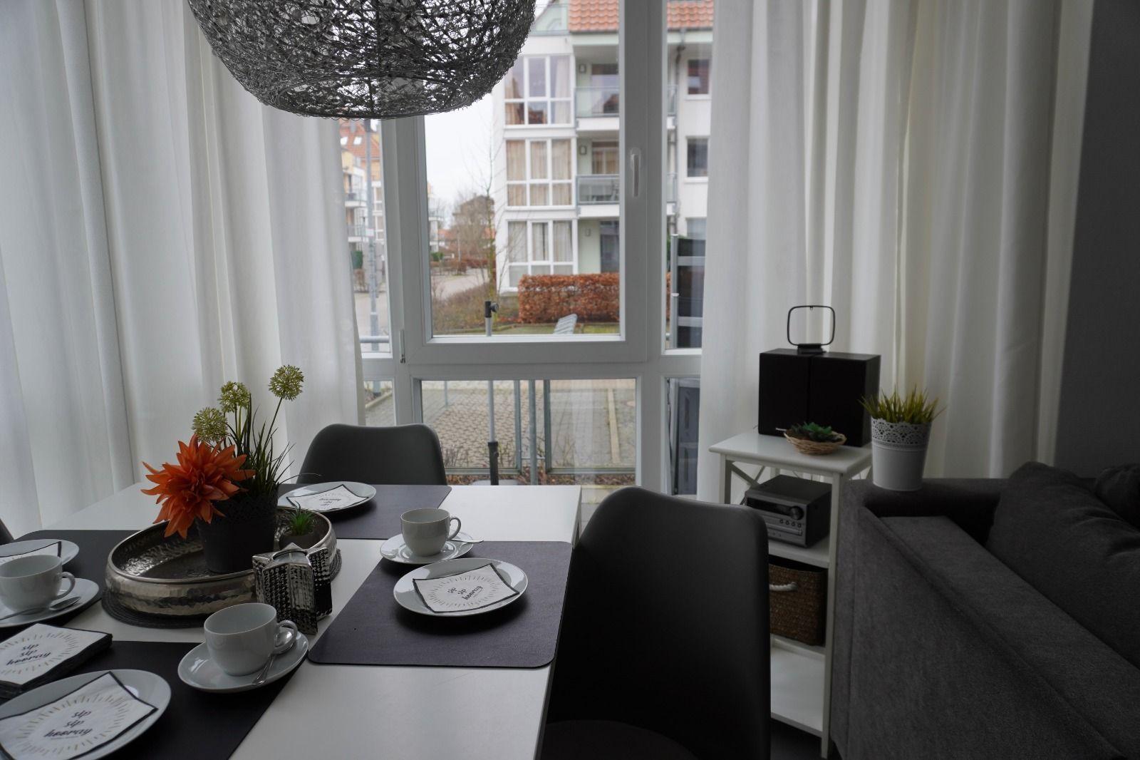 Esstisch mit Stühlen, Sofa und Fensterblick auf Außenbereich.