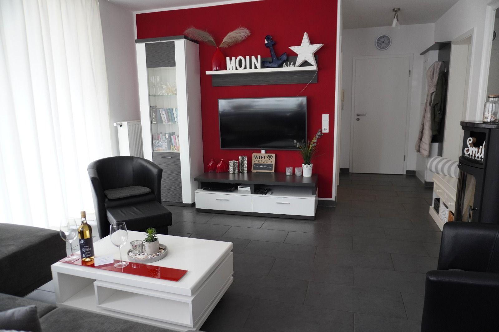 Wohnzimmer mit roter Wand, TV, Couch und Tisch.