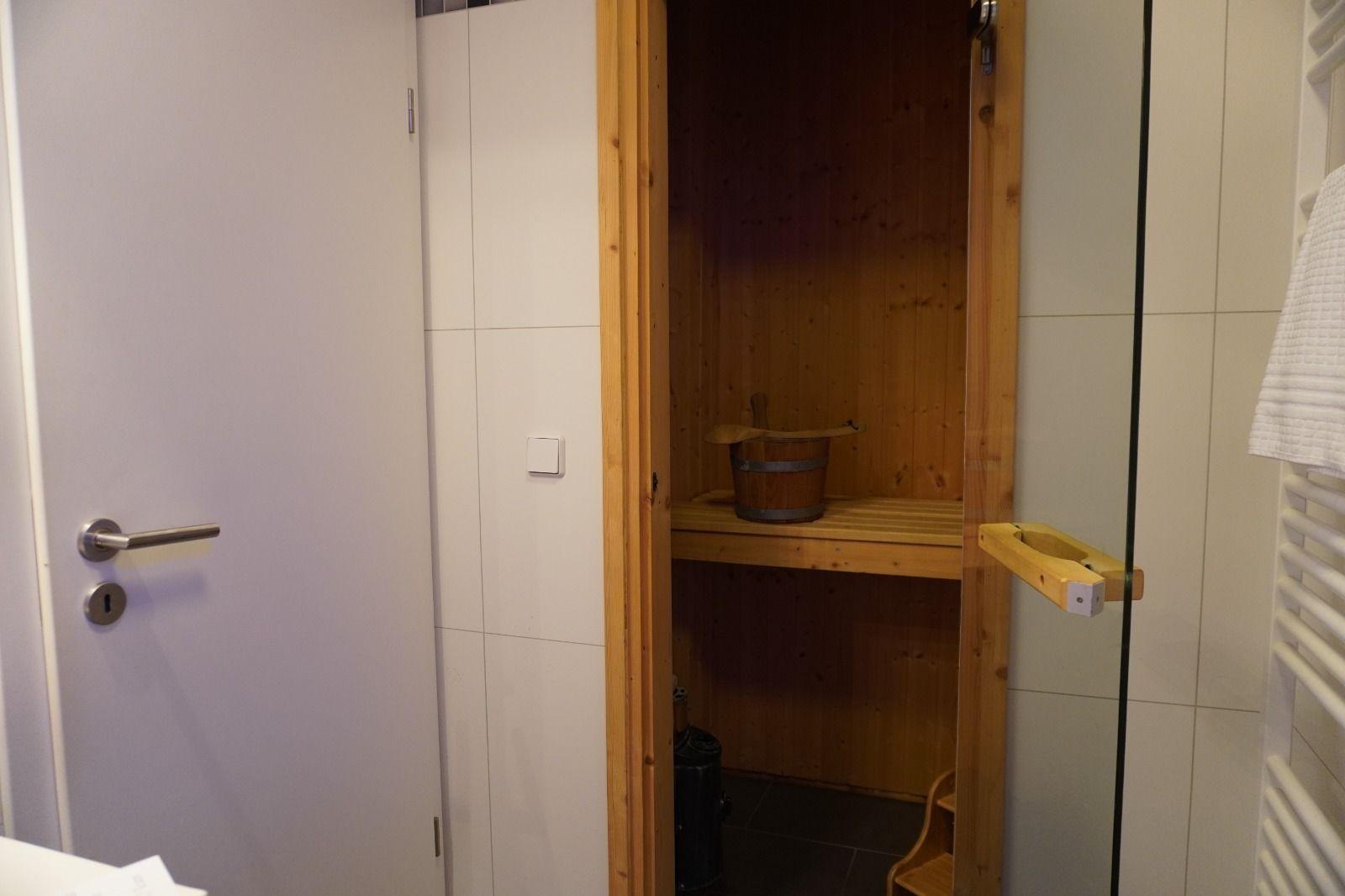 Sauna mit Holzbank und Eimer, getrennt durch Glaswand.