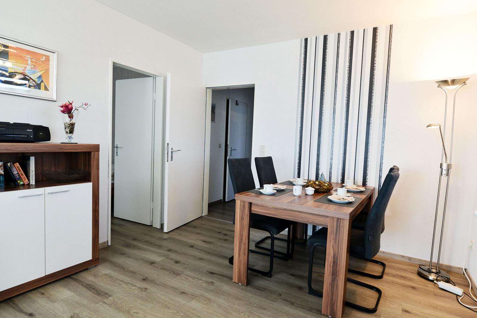 Essbereich mit Tisch, Stühlen und Wandtapete. Holzboden und Schrank sichtbar.