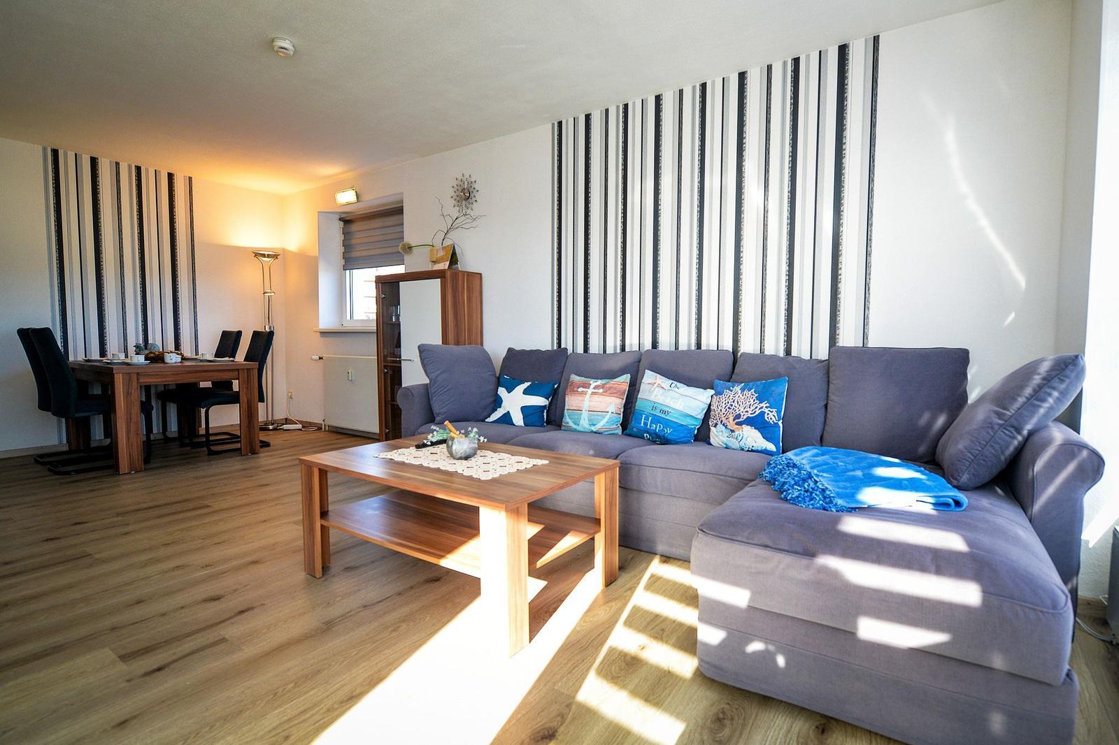 Ein Wohn- und Essbereich mit grauem Sofa, Holztisch und gestreifter Wand.