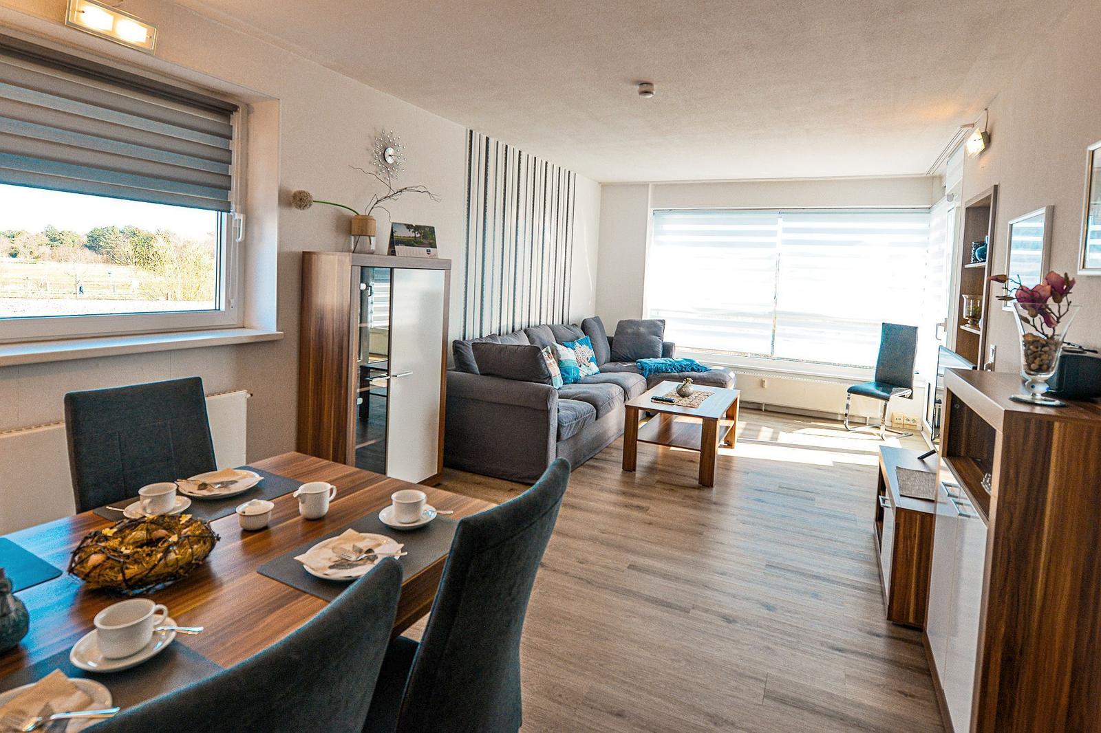 Wohn- und Essbereich mit Sofa, Tisch und Stühlen. Holzboden und große Fenster.