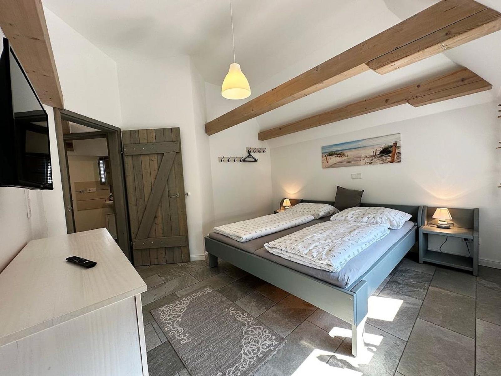 Schlafzimmer mit Doppelbett, Holzbalken und TV. Tür führt in Bad.