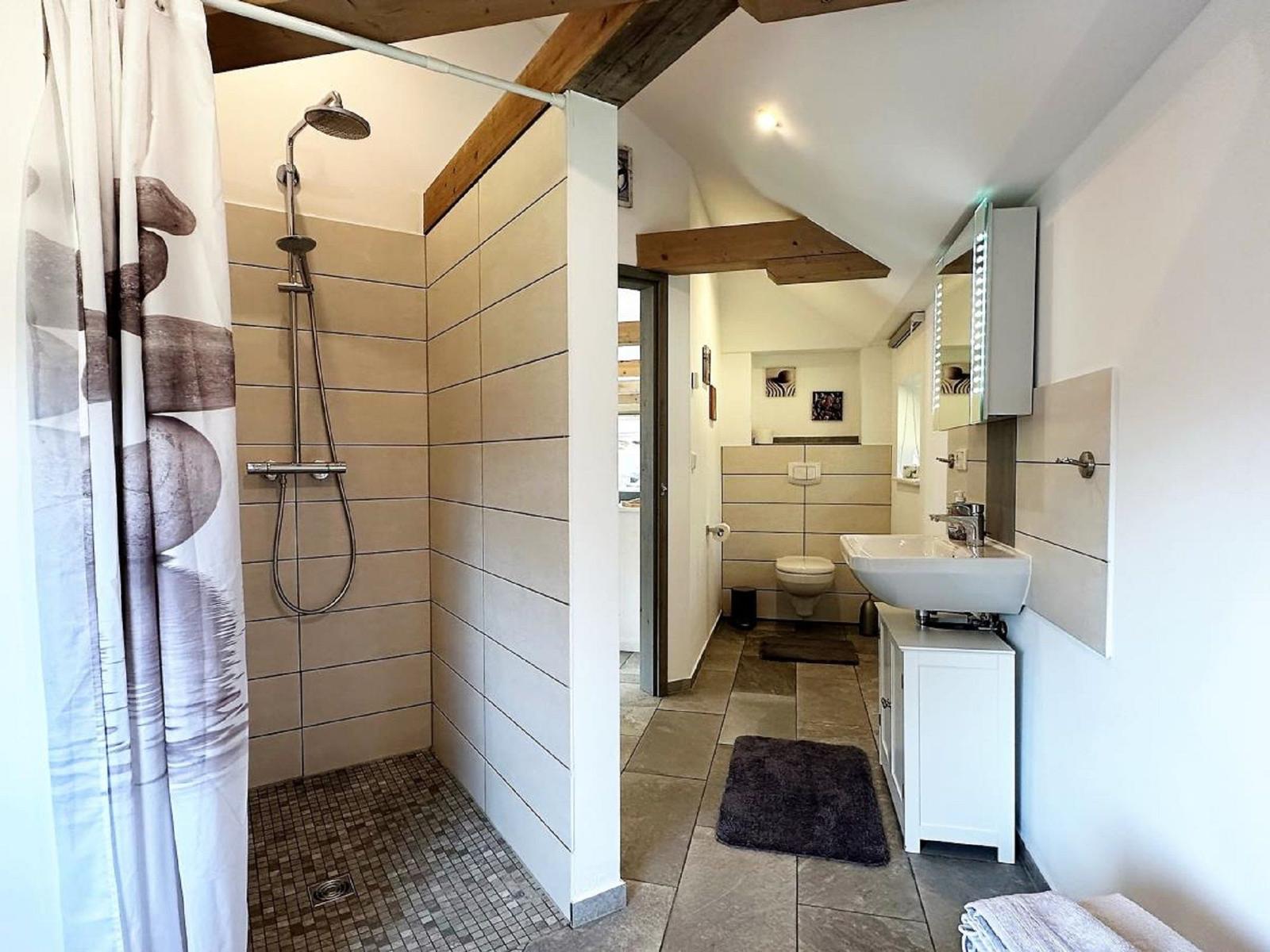 Badezimmer mit Dusche, Waschbecken und Toilette. Holzbalken an der Decke.