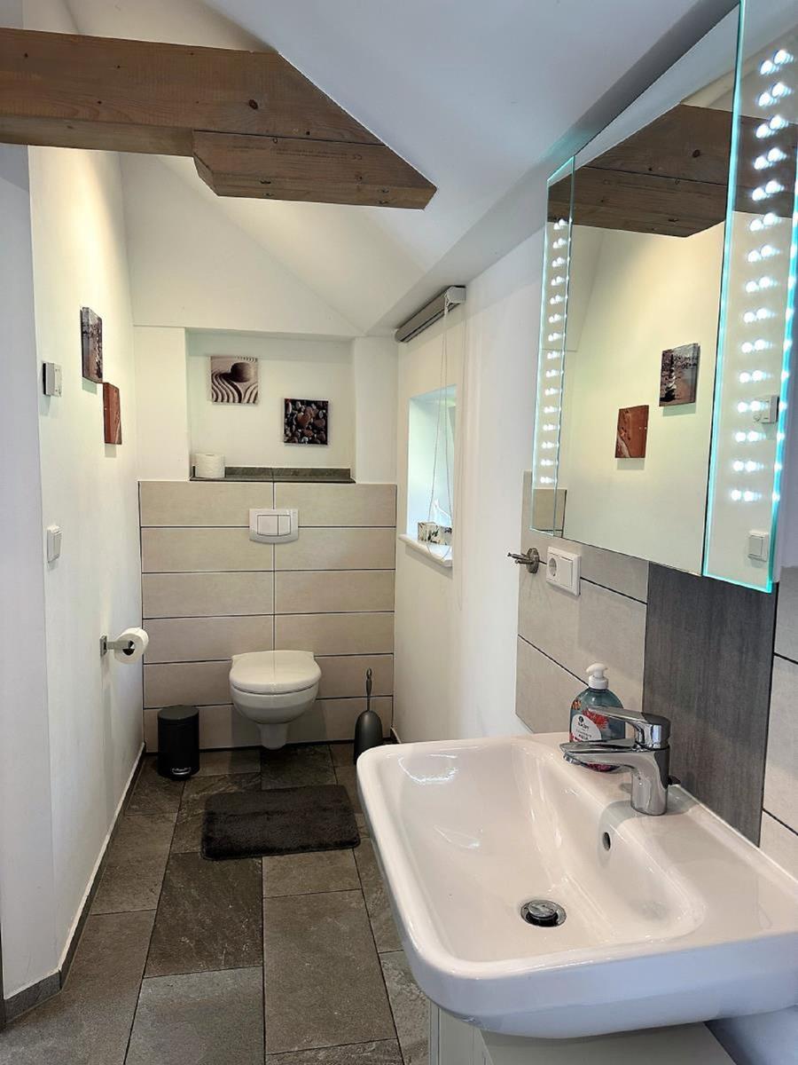Badezimmer mit Waschbecken, Spiegel und Toilette unter Holzbalken.