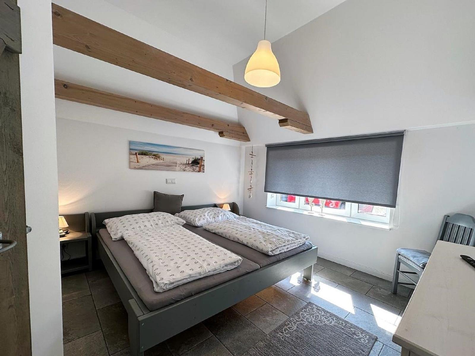 Schlafzimmer mit Doppelbett, Holzbalken und Fenster mit Rollladen.