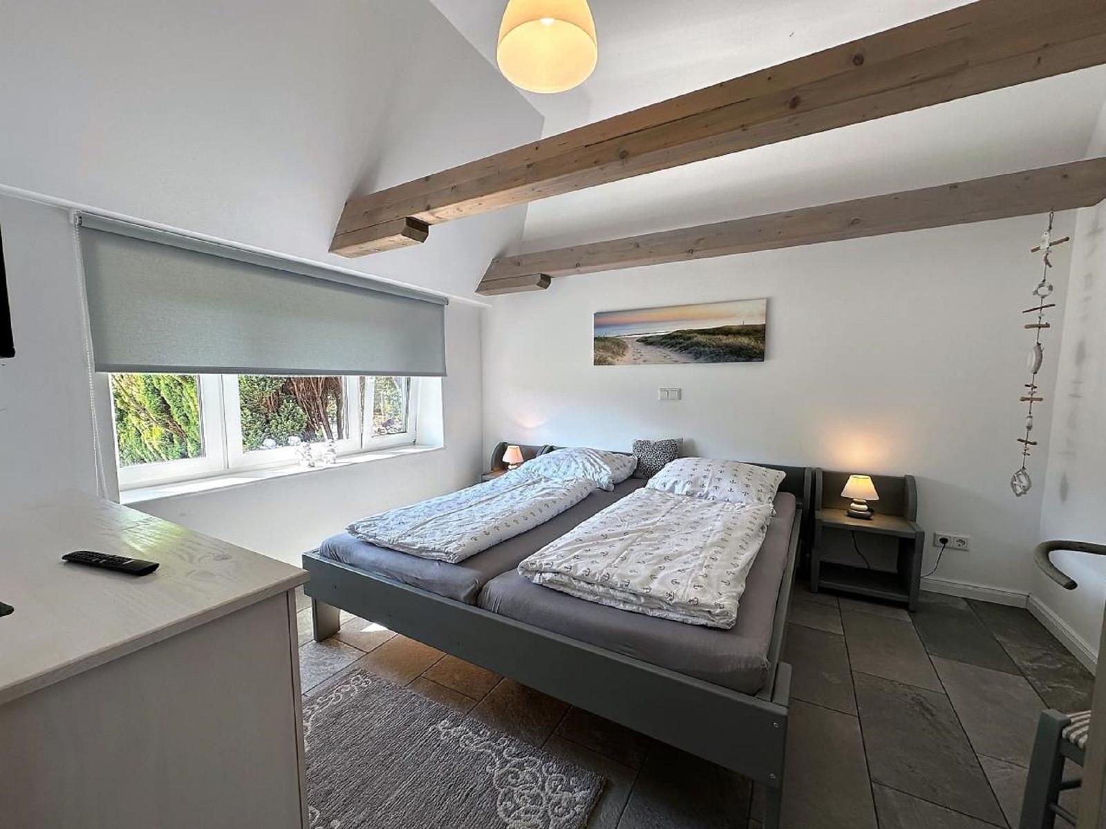 Schlafzimmer mit Doppelbett, Fenster und Holzbalken an der Decke.