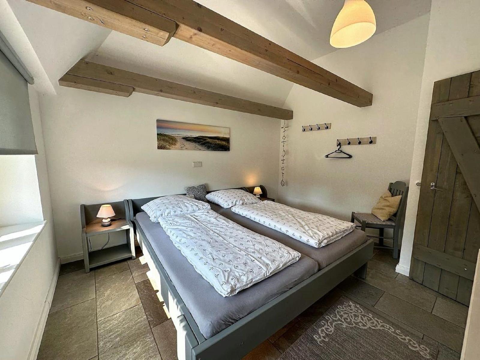 Schlafzimmer mit Doppelbett, Holzbalken, Nachttisch und Stuhl.