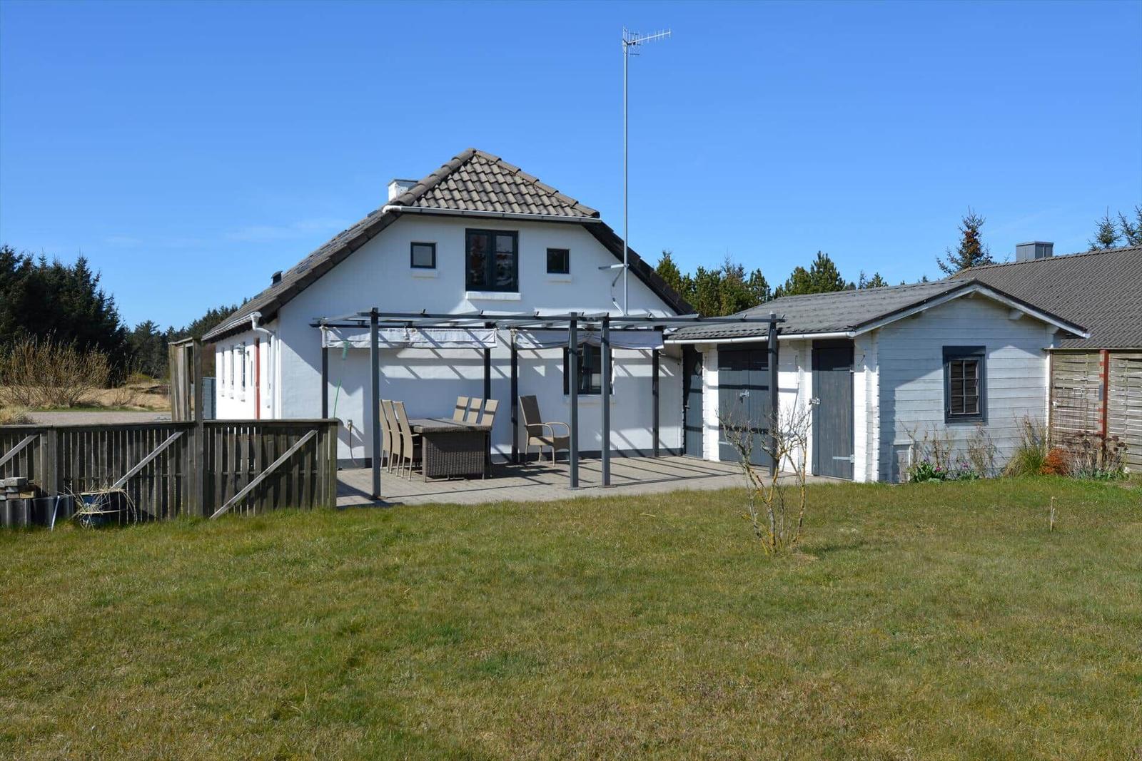 Wohnhaus mit Terrasse und Garten. Außentisch mit Stühlen. Hintergrund: Wald und klarer Himmel.