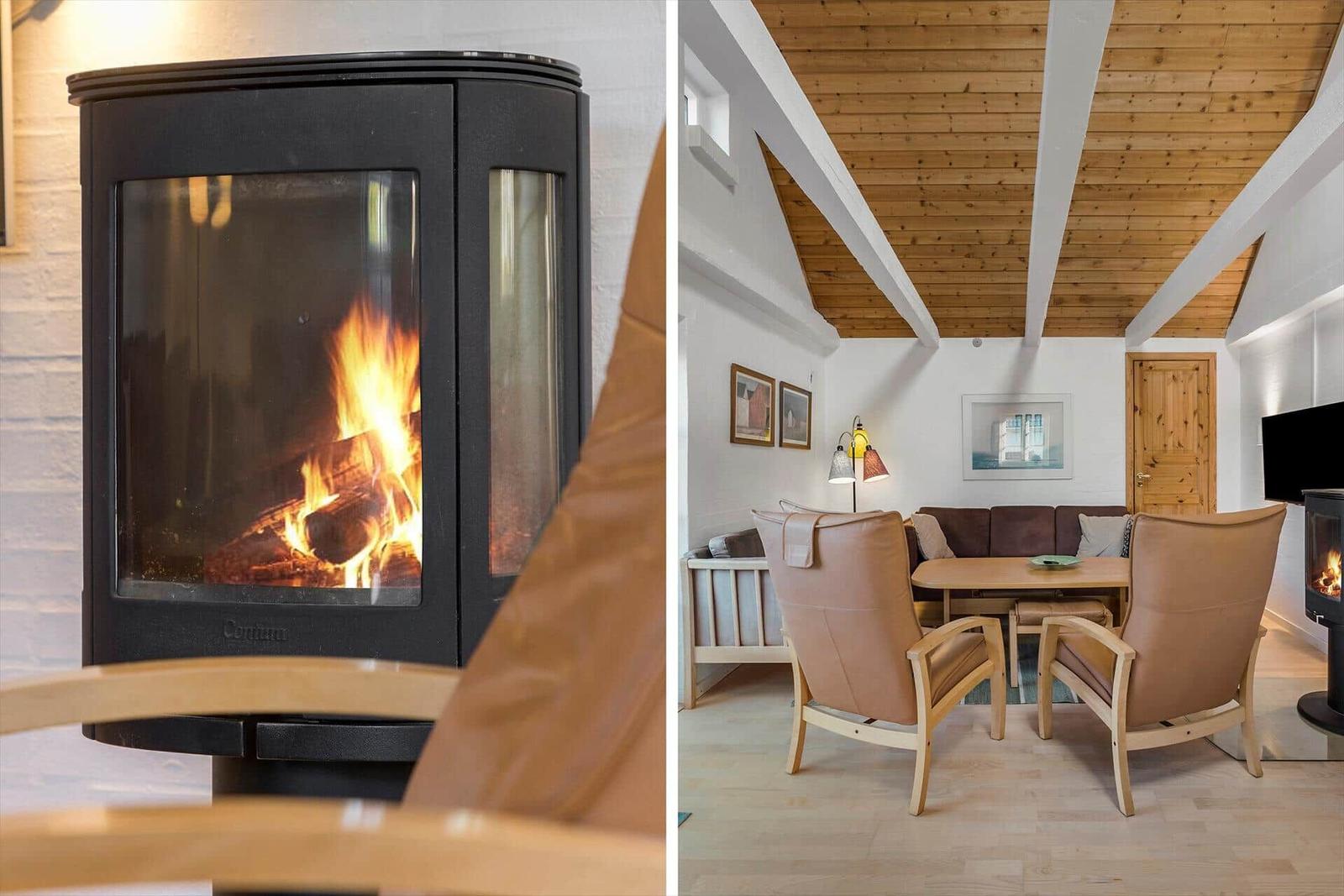 Kaminofen mit brennendem Holz. Wohnzimmer mit Sitzgruppe, Tisch und Holzbalkendecke.