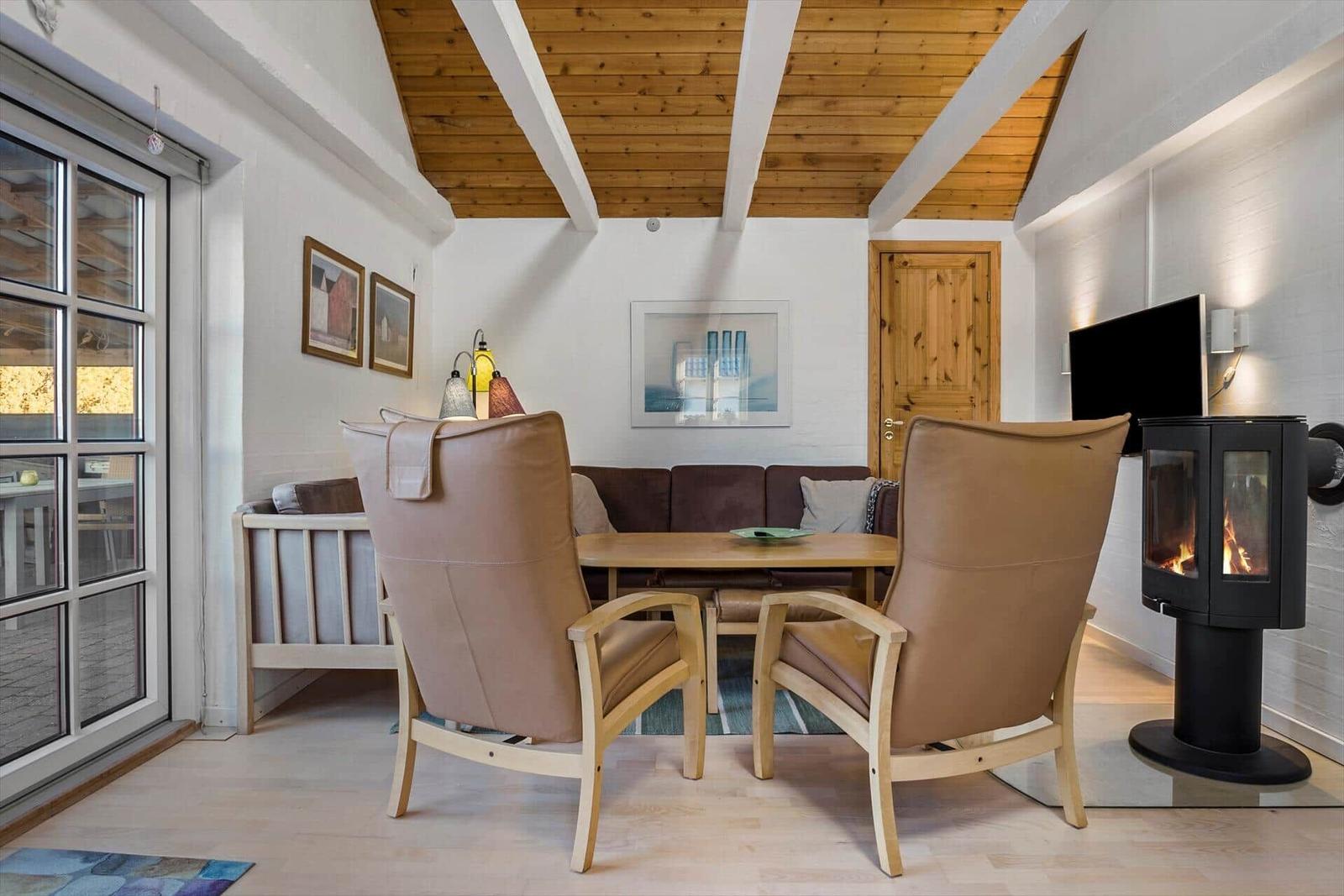 Wohnzimmer mit Holzdecke, Sitzgelegenheiten und Kaminofen.