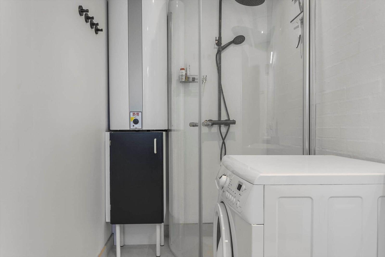 Dusche mit Duschbrause, Waschmaschine und Heizungsgerät im Badezimmer.