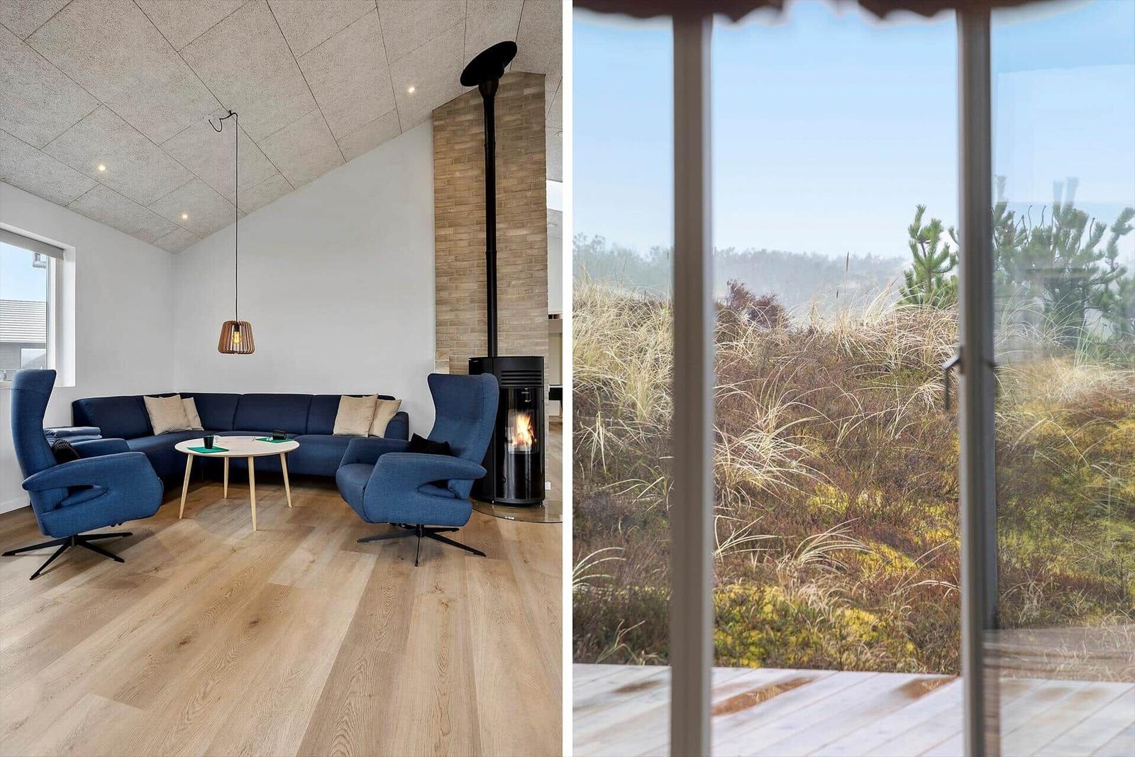 Wohnzimmer mit blauer Couch und Kamin. Aussicht auf Grasland und Bäume.