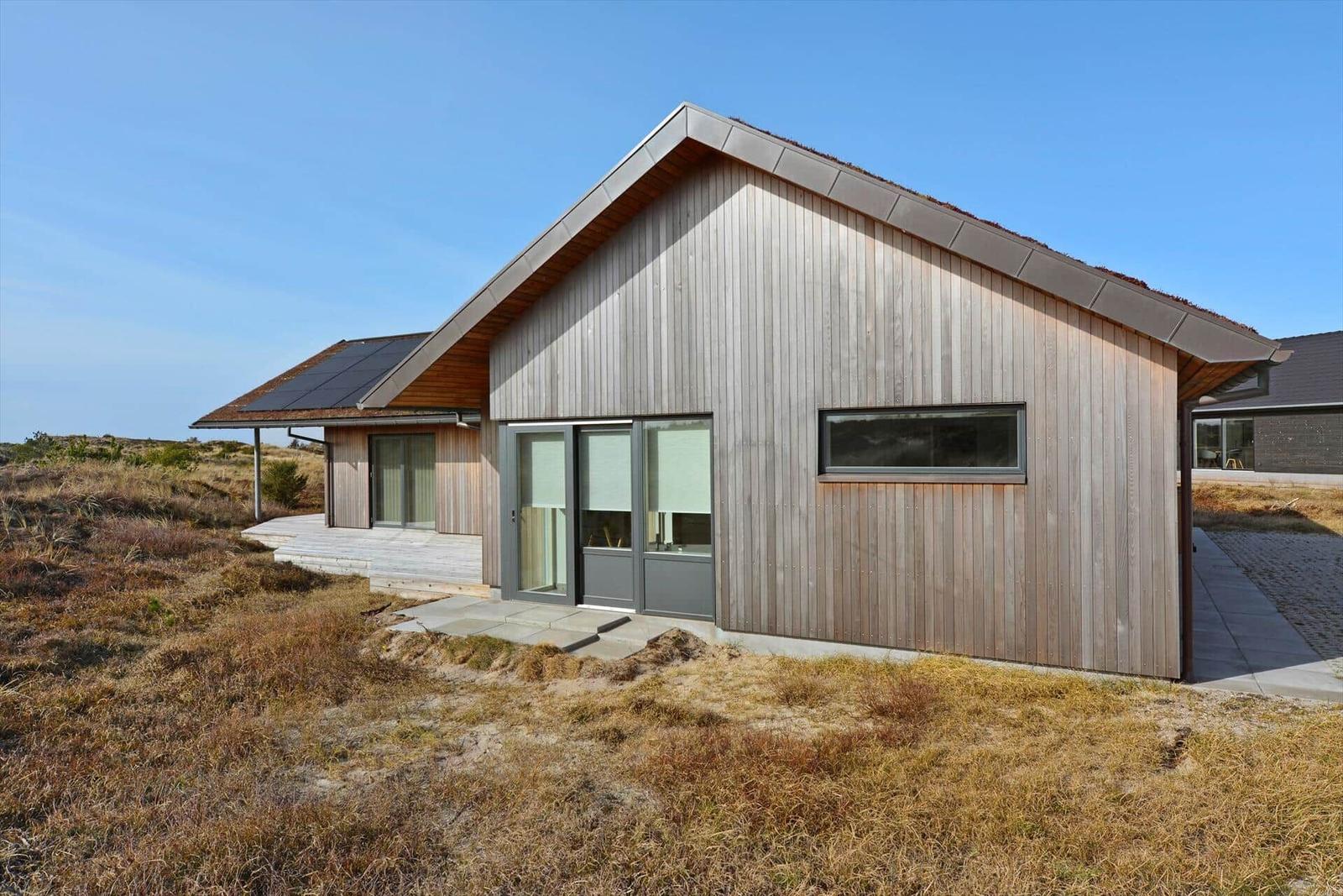 Moderne Holzhütte mit Glasfront und Solaranlage auf grasigem Grund.
