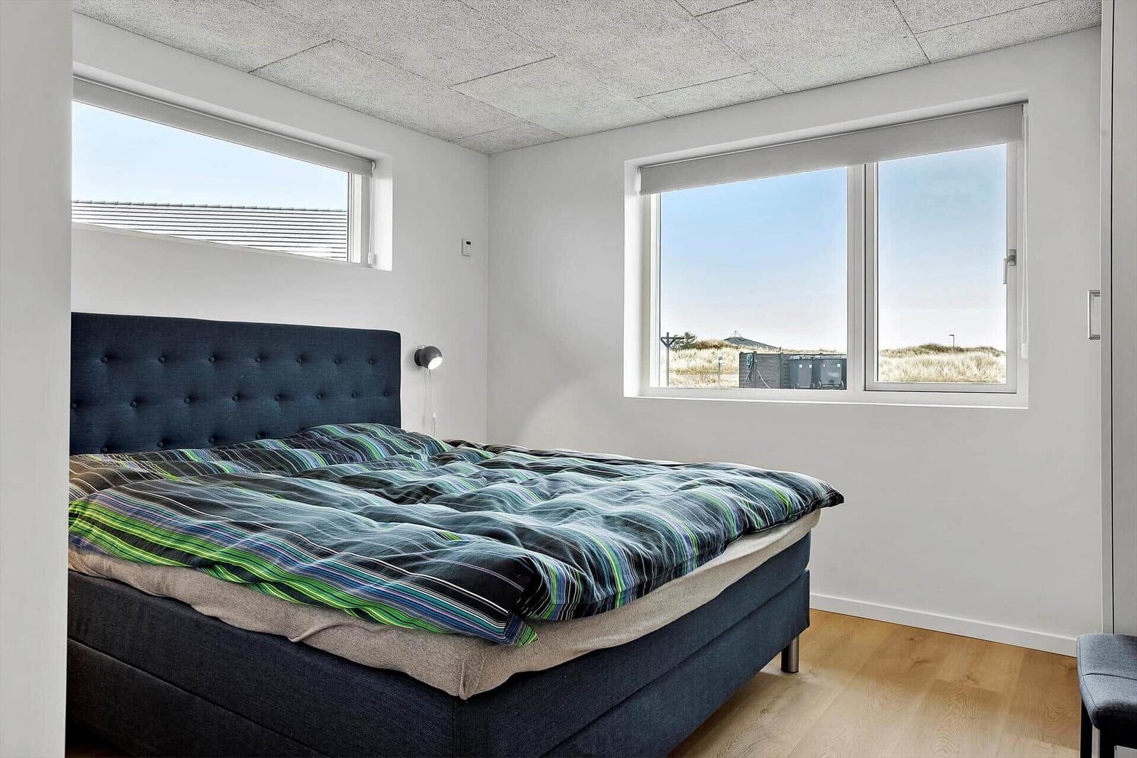 Schlafzimmer mit Bett, Fenstern und Holzboden.