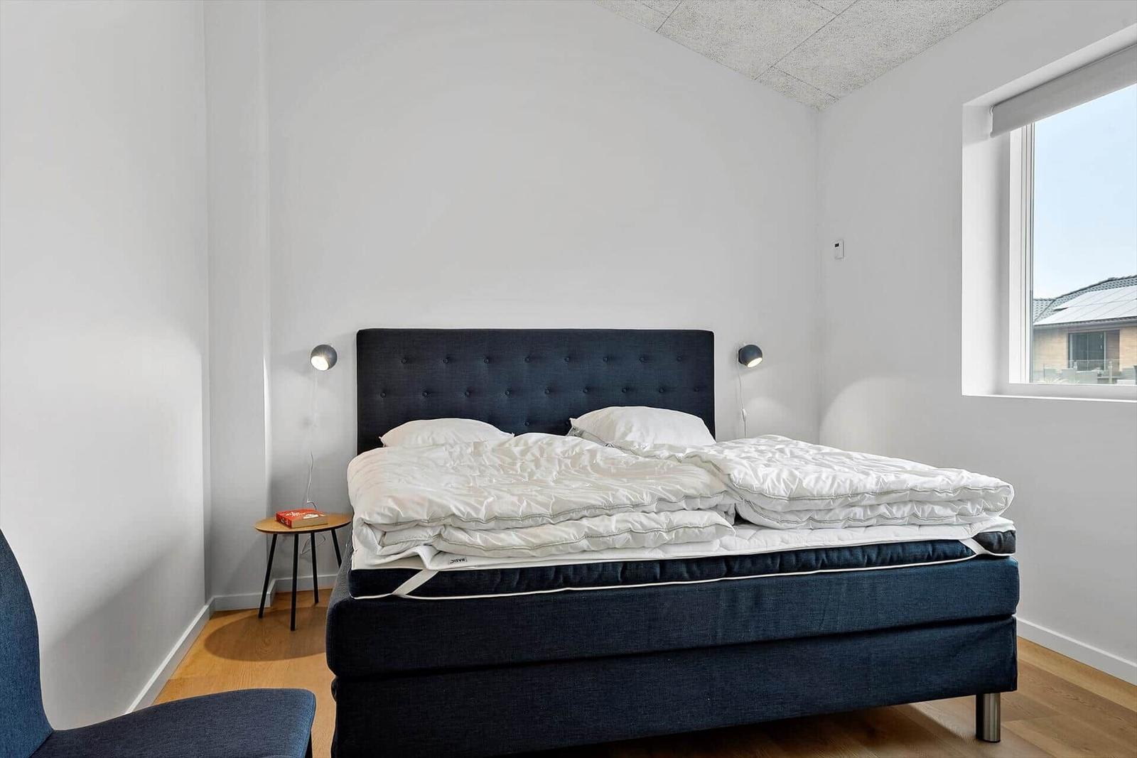Schlafzimmer mit Doppelbett, dunklem Kopfteil und Fenster