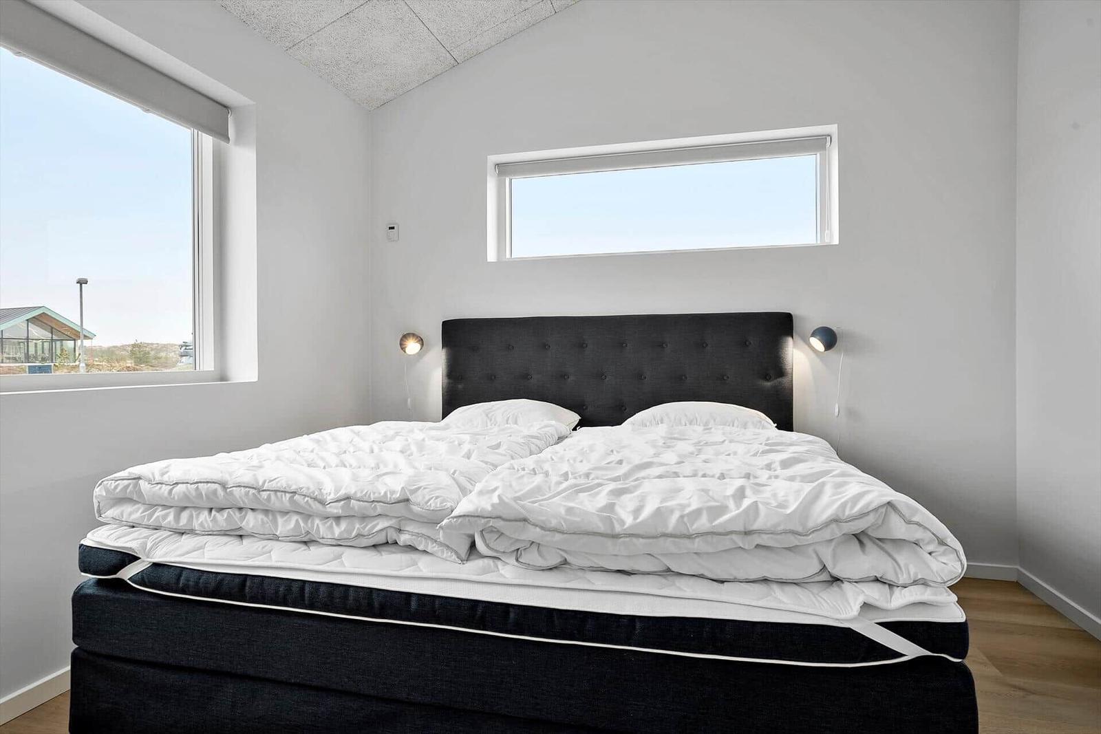 Schlafzimmer mit großem Bett, zwei Fenstern und Wandlampen.