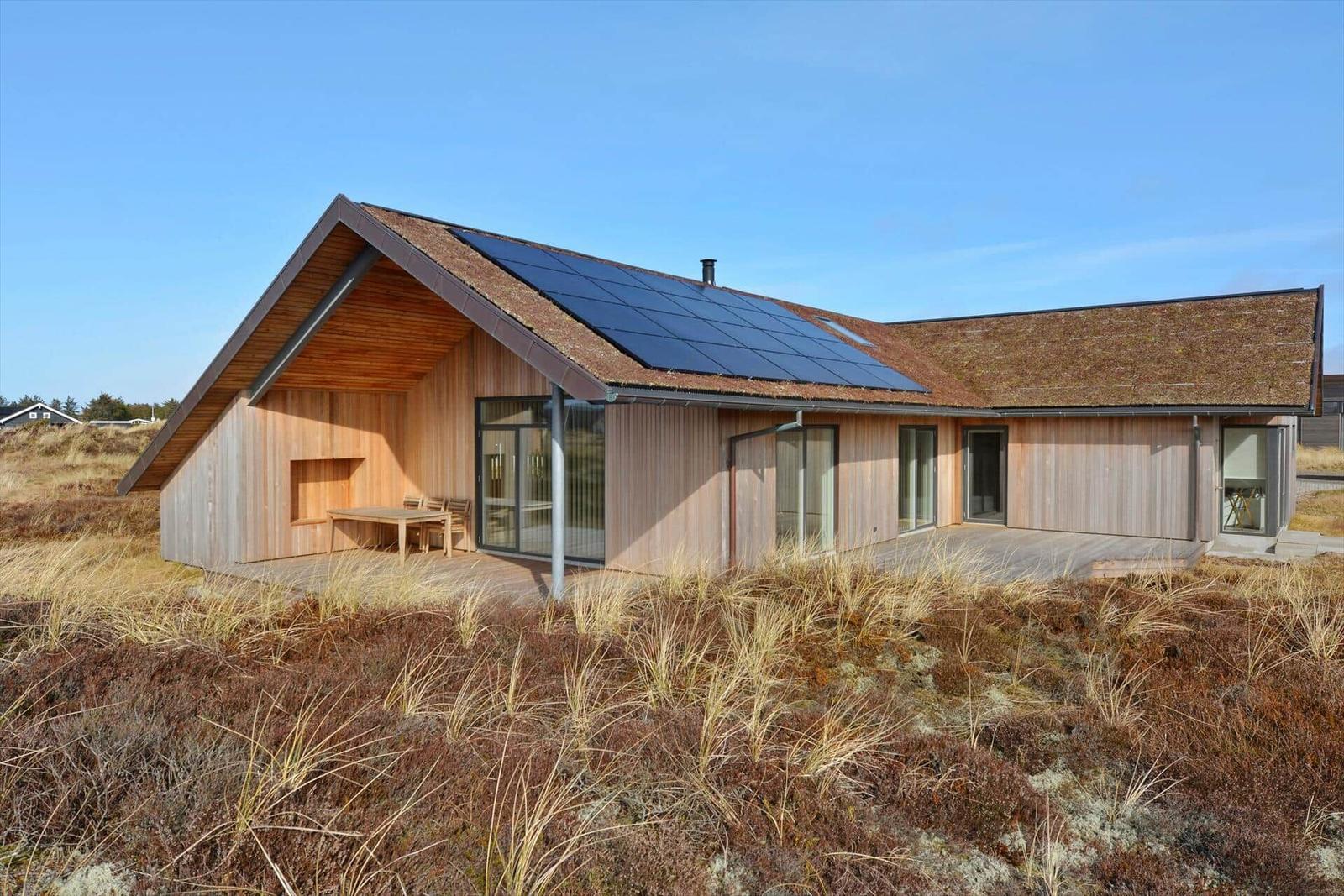 Moderne Holzhütte mit Solarpaneelen und großzügigen Glasflächen im Freien.