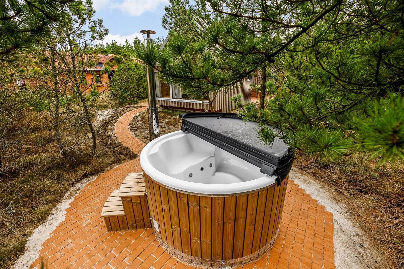 Ein Whirlpool mit Holzrahmen auf einem Kiesweg zwischen Bäumen.