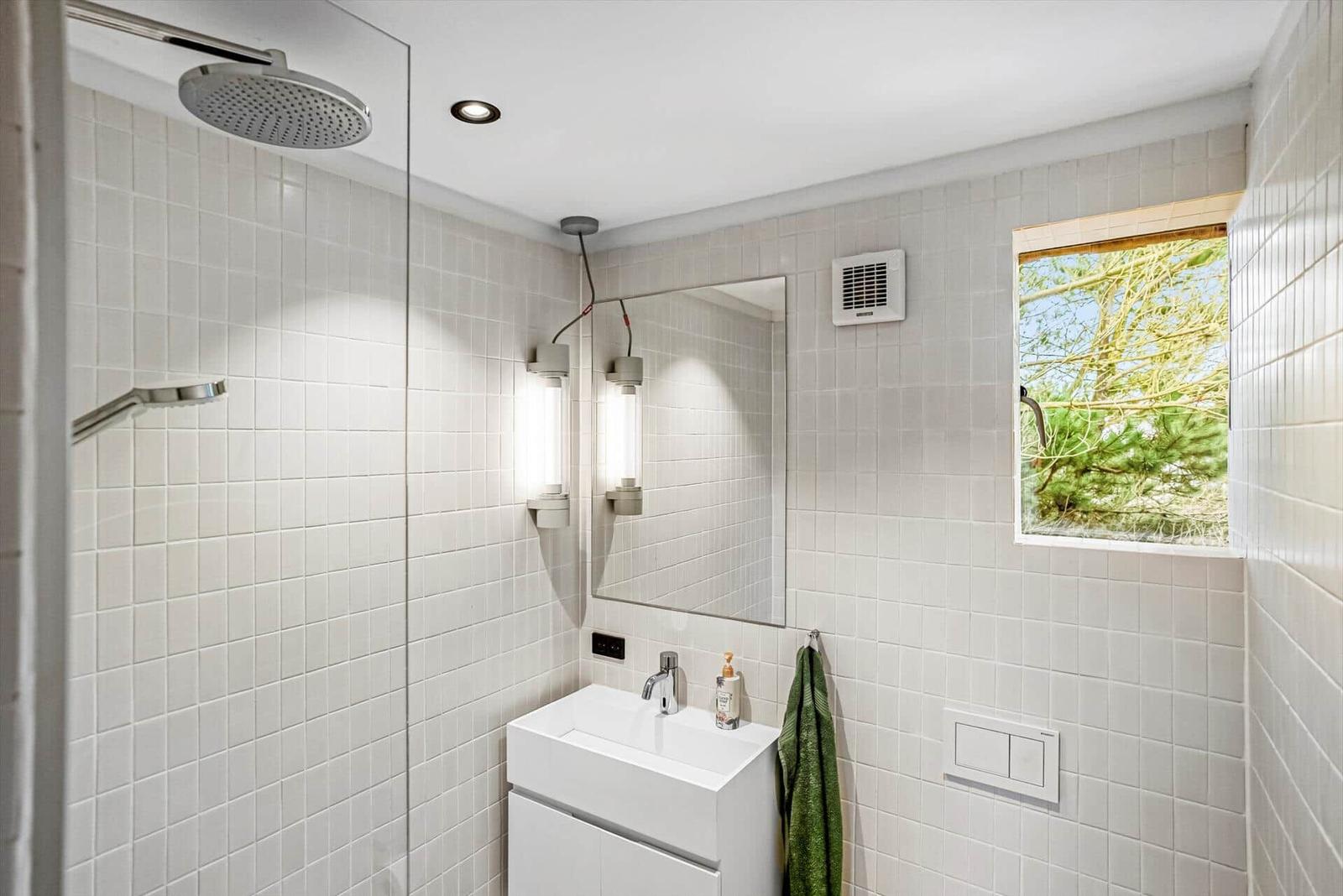 Badezimmer mit Dusche, Waschbecken und Fenster zum Garten.