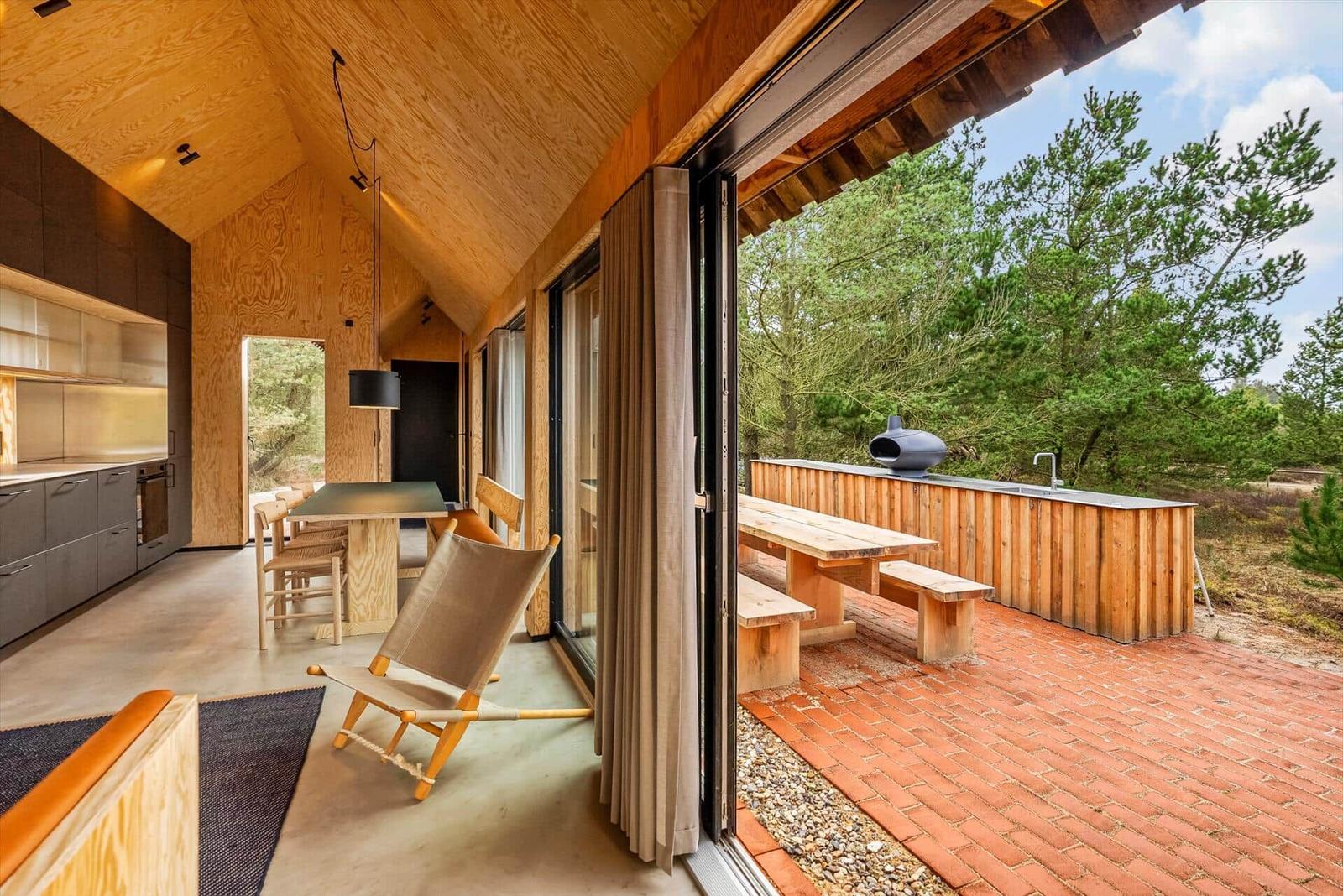 Haus mit Holzverkleidung, Küche, Essbereich und Terrasse mit Grill und Bänken.