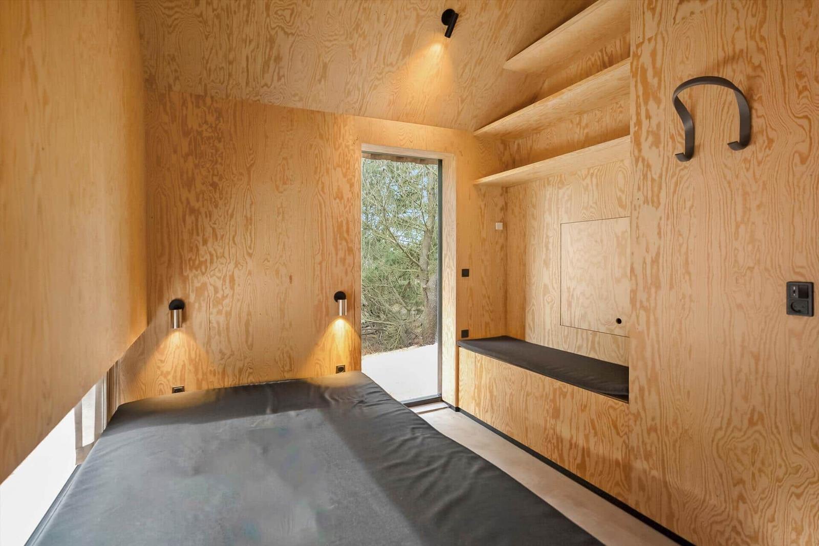 Schlafzimmer mit Holzwand, Bett und Fenster zur Außenseite.