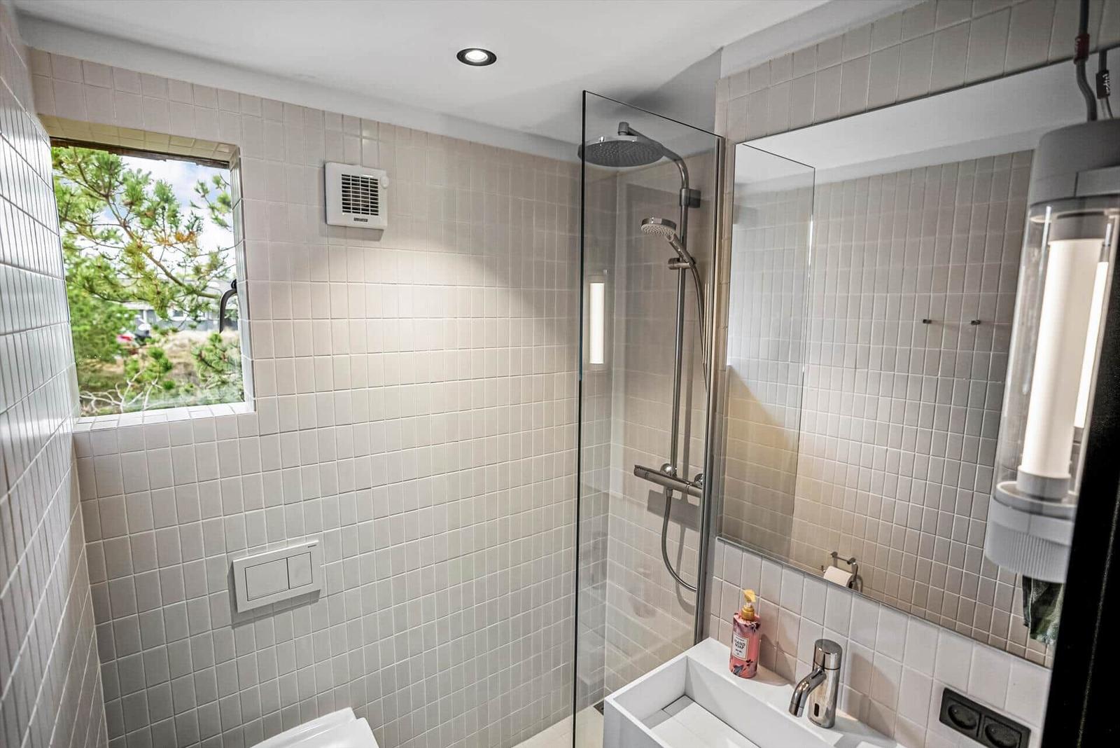 Badezimmer mit Dusche, Waschbecken und Fenster mit Blick auf Grün.
