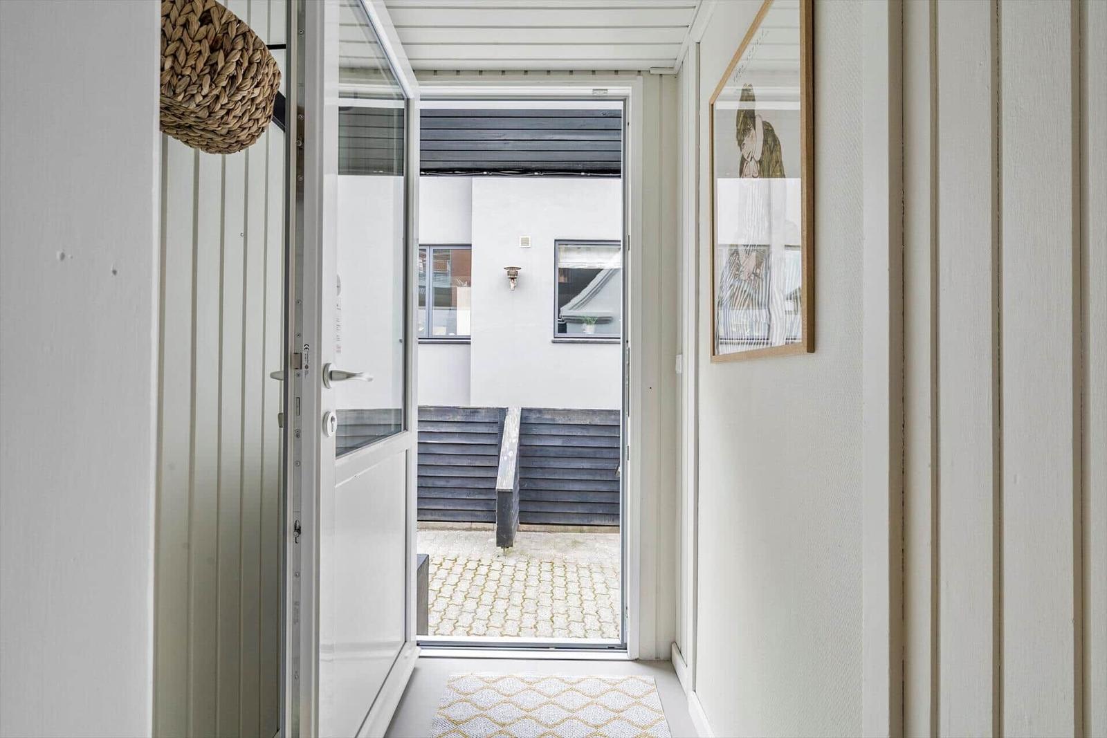 Hausgang mit offener Tür zum Hof mit Steinplatten und dunklem Holzgeländer.