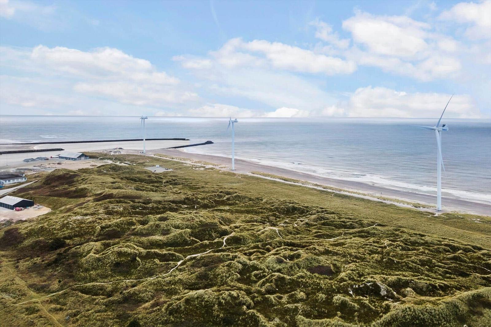 Strand mit Dünen und Windkraftanlagen am Horizont.