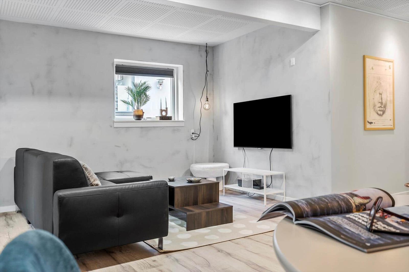 Wohnzimmer mit Sofa, Fernseher und Fenster. Holzboden und Wandgestaltung.