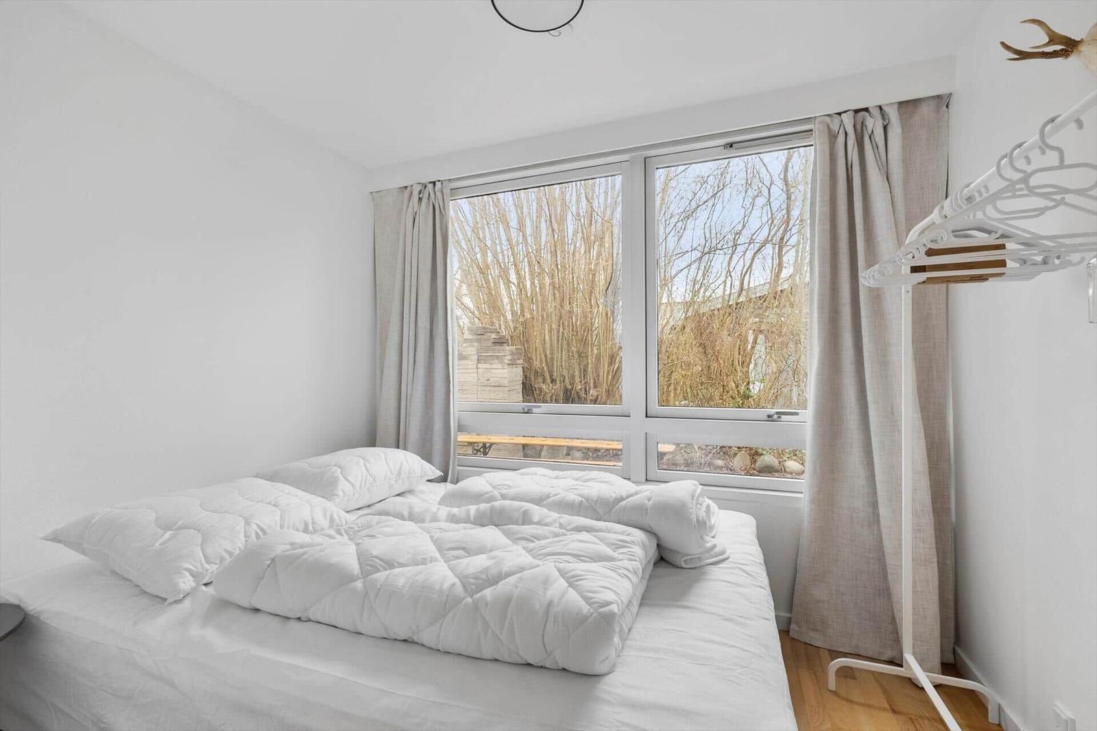 Schlafzimmer mit weißem Bett, Fenster und Gardinen.